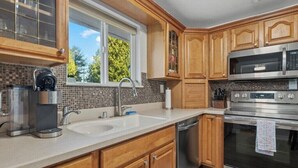 Una cocina con armarios de madera, un lavamanos doble, una cafetera y electrodomésticos de acero inoxidable.