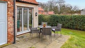 A patio with a table and chairs, a brick wall, and a glass door leading to a covered area. - Escape to this picturesque retreat in Salton, near Malton. (Salton, near Malton)