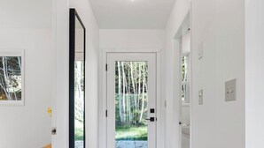 Un couloir doté d’un plancher en bois, d’un tapis à motifs, d’un banc et d’une porte donnant sur un espace extérieur agrémenté de bambous.