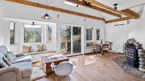 Un salon spacieux doté d’un plafond en bois, de grandes fenêtres, d’une cheminée et d’un coin salon confortable.