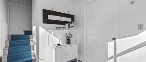 A staircase with blue steps leading to a landing with a white wall, a black-framed mirror, and a small potted plant.