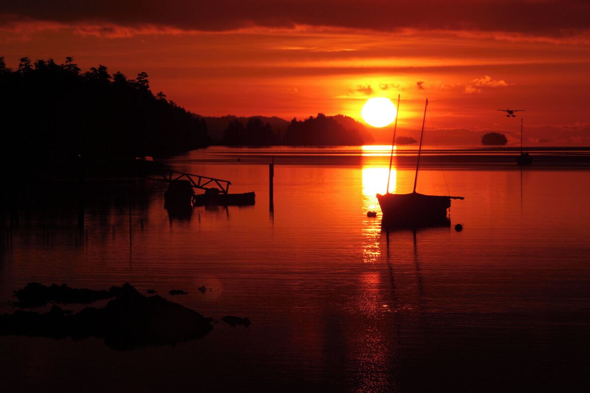 Un atardecer sobre un lago tranquilo, con un bote y un muelle en primer plano.