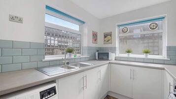 A kitchen with white cabinets, a microwave, a sink, and two windows with potted plants.