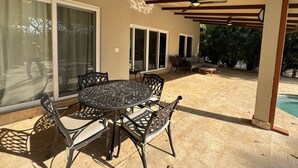 An outdoor patio with a round table and chairs, a ceiling fan, and a pool in the background.