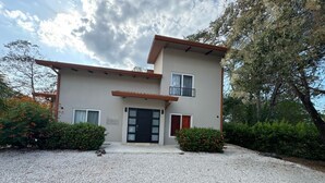 A two-story house with a gravel driveway, a black front door, and a small balcony on the upper floor.