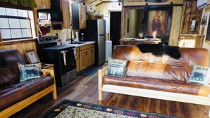 Een gezellig interieur van een chalet met een bruine leren bank, een houten eettafel en een keukenhoek.