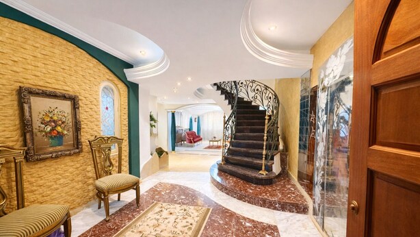 Un amplio pasillo con suelo de mármol, una escalera con barandillas decorativas y una gran puerta de madera.
