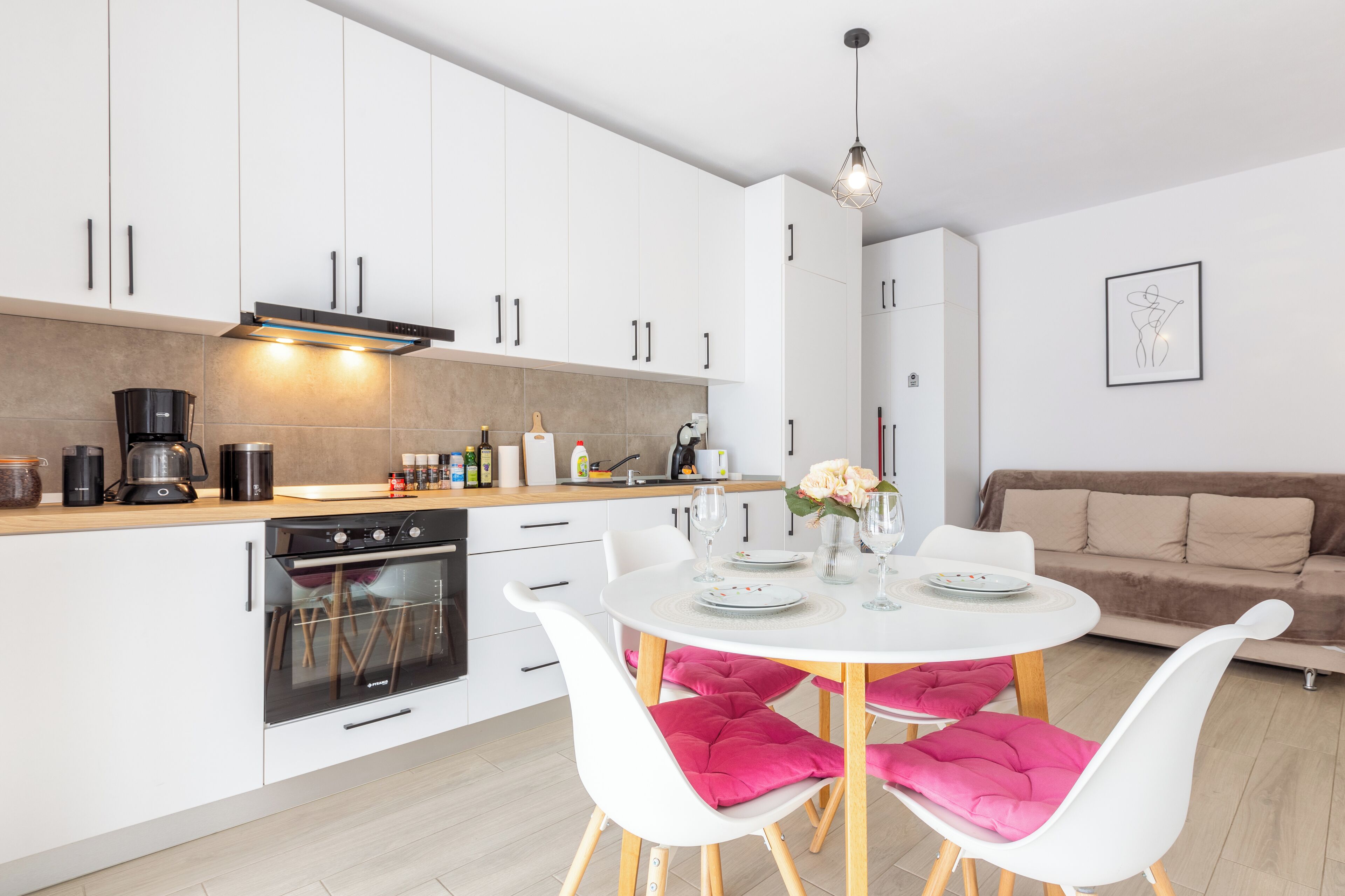 A modern kitchen with white cabinets, a built-in oven, and a dining area with a white table and chairs.