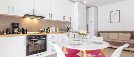 A modern kitchen with white cabinets, a built-in oven, and a dining area with a white table and chairs.