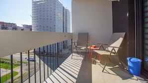 A balcony with a view of a building under construction, a chair, a small table, and a trash bin. - ATENEO - Studio DeLuxe MODERN Apartment, BIG Balcony, Plus FREE Parking (Timișoara)