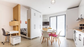 A modern kitchen with white cabinets, a dining area with a table and chairs, and a built-in desk with a chair. - ATENEO - Studio DeLuxe MODERN Apartment, BIG Balcony, Plus FREE Parking (Timișoara)