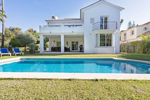 A two-story house with a swimming pool, a covered patio, and a garden.