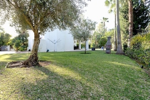 A well-maintained garden with a large tree, a white building, and a stone structure.