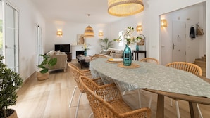 A spacious living area with a dining table, wicker chairs, and a large hanging light fixture.