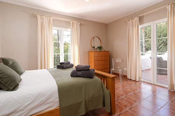 A bedroom with a bed, a wooden dresser, and a view through a sliding glass door.