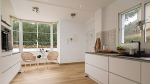 A modern kitchen with white cabinets, a wooden countertop, and a large window with a view of greenery.