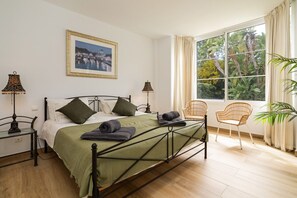 A bedroom with a bed, two bedside tables, a window with curtains, and a chair.