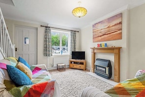 Una sala de estar con sofá, televisión, chimenea y un cuadro en la pared.