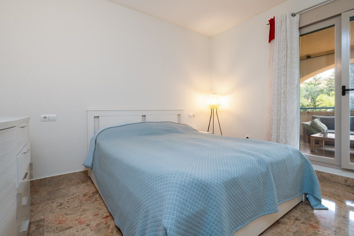 A bedroom with a bed, a nightstand, a lamp, and a sliding glass door leading to an outdoor area.