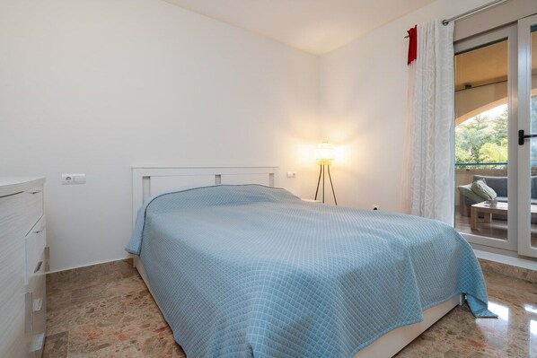 Un dormitorio con cama, mesita de noche, lámpara y puerta corrediza de vidrio que da a un espacio exterior.