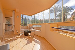 A spacious room with a large window, a seating area with a sofa and chairs, and a view of palm trees and buildings.