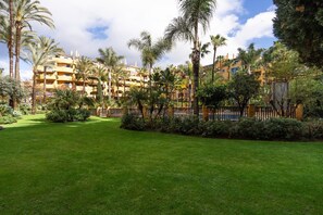 Un patio de hotel con césped cuidado, palmeras y una cerca.