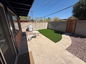 Ein Garten mit Kunstrasen, einem Grill und Gartenmöbeln.
