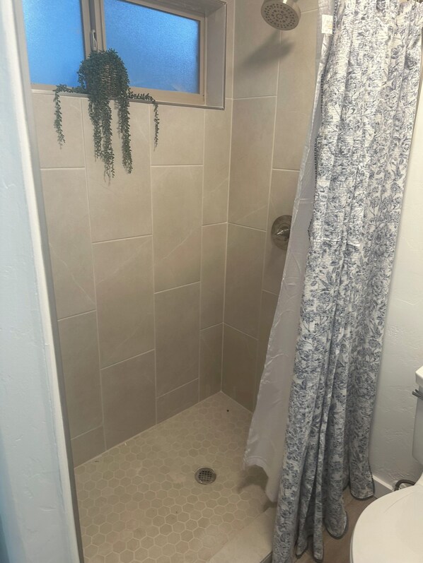 Un pequeño rincón de ducha con azulejos, una ventana y cortina.