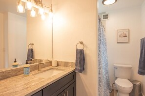 Ein Badezimmer mit Waschbecken, Spiegel, Handtuchhalter, Toilette und Duschvorhang.