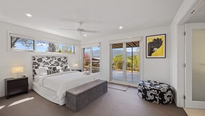 Un dormitorio con una cama grande, un ventilador de techo, un banco, una ventana con vistas y un cuadro en la pared.