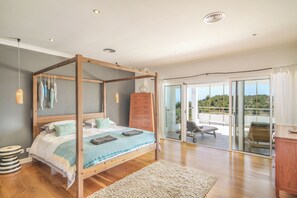 Relax in a serene bedroom with a four-poster bed, sliding glass door to a balcony, and a comfortable nightstand.