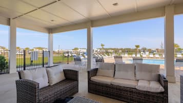 Relax in a shaded outdoor seating area with wicker sofas and a nearby swimming pool.