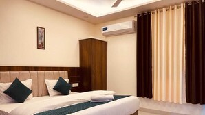 A hotel room with a large bed, a wardrobe, an air conditioning unit, and a window with curtains. - Hotel Divine Ganga (Haridwar)