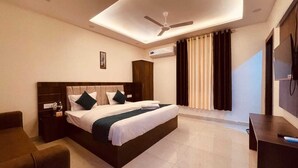 A modern hotel room with a large bed, a desk, a chair, a ceiling fan, and a TV. - Hotel Divine Ganga (Haridwar)