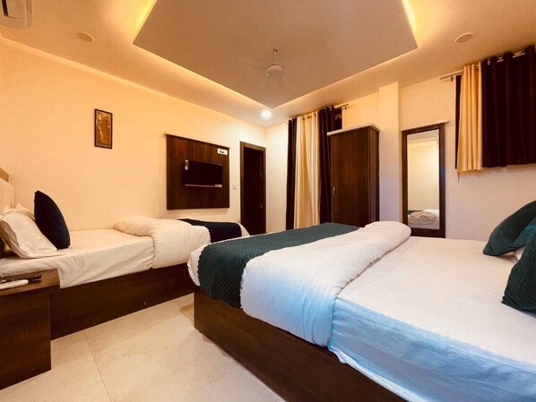 A modern hotel room with a large bed, a smaller bed, a desk with a lamp, a TV, and a wardrobe.