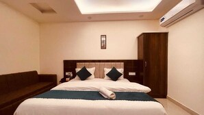 A hotel room with a bed, a dark-colored sofa, a wooden wardrobe, and an air conditioning unit. - Hotel Divine Ganga (Haridwar)