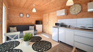 A compact wooden cabin with a kitchenette, a dining area, and a living space with a sofa and cushions. - Holiday Homes Close to the Beach, Large Playground (Mielno)