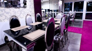 A modern dining area with black tables, white chairs, and a purple accent wall. - Palermó Panzió (Nyíregyháza)
