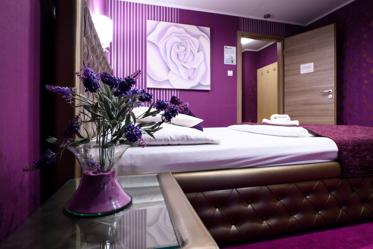 A hotel room with a bed, a vase of flowers, a mirror, and a door.