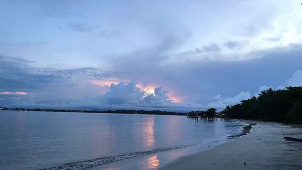 A beach with calm waters reflecting the sky, a sandy shore, and a distant structure. - Seahouse Beachfront B&B with Pool (Bocas del Toro)