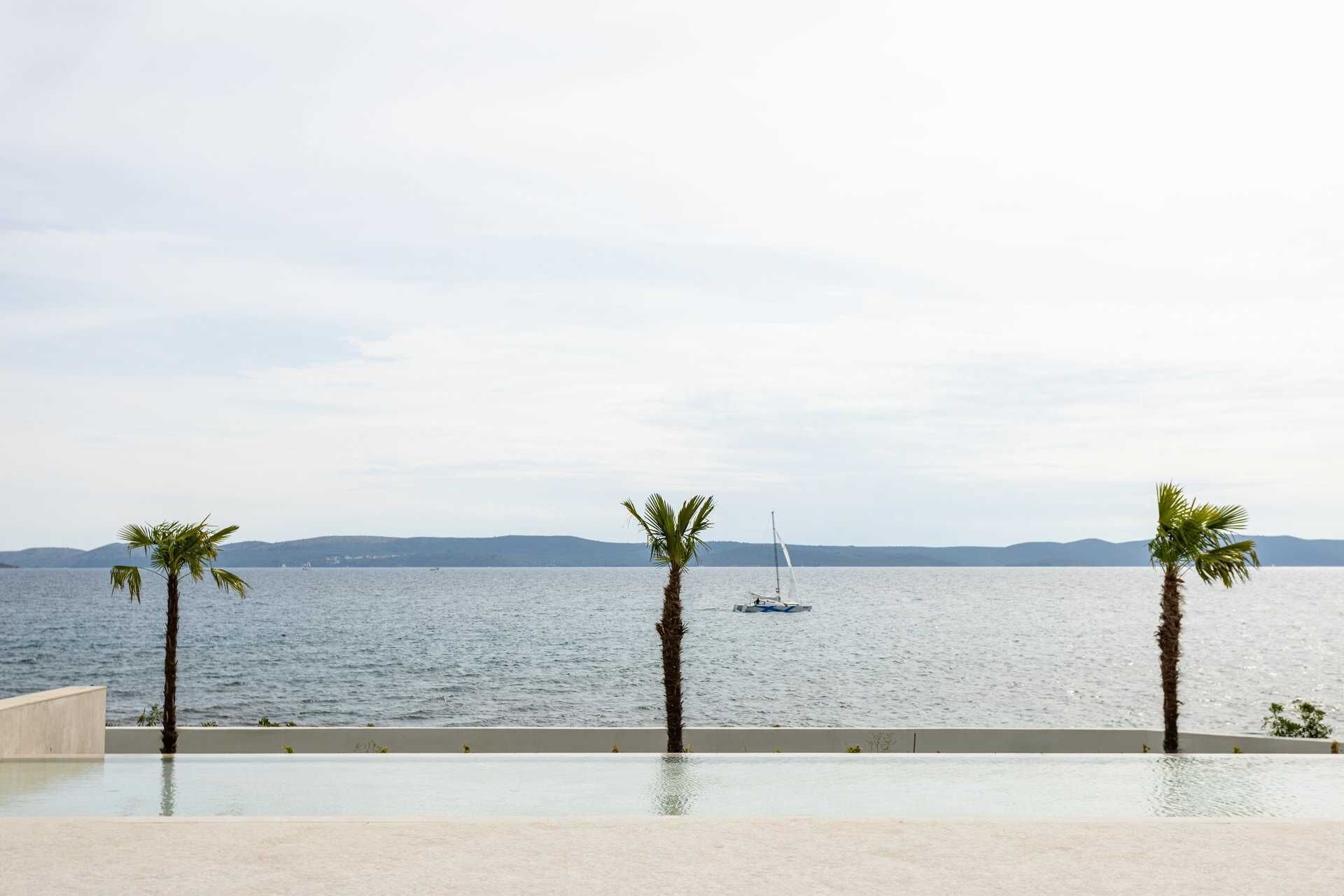 Une vue sur la piscine, avec une mer calme, un voilier et des collines à l’horizon.