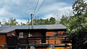 Una cabaña de troncos con terraza, mobiliario exterior y un hogar para fogata.