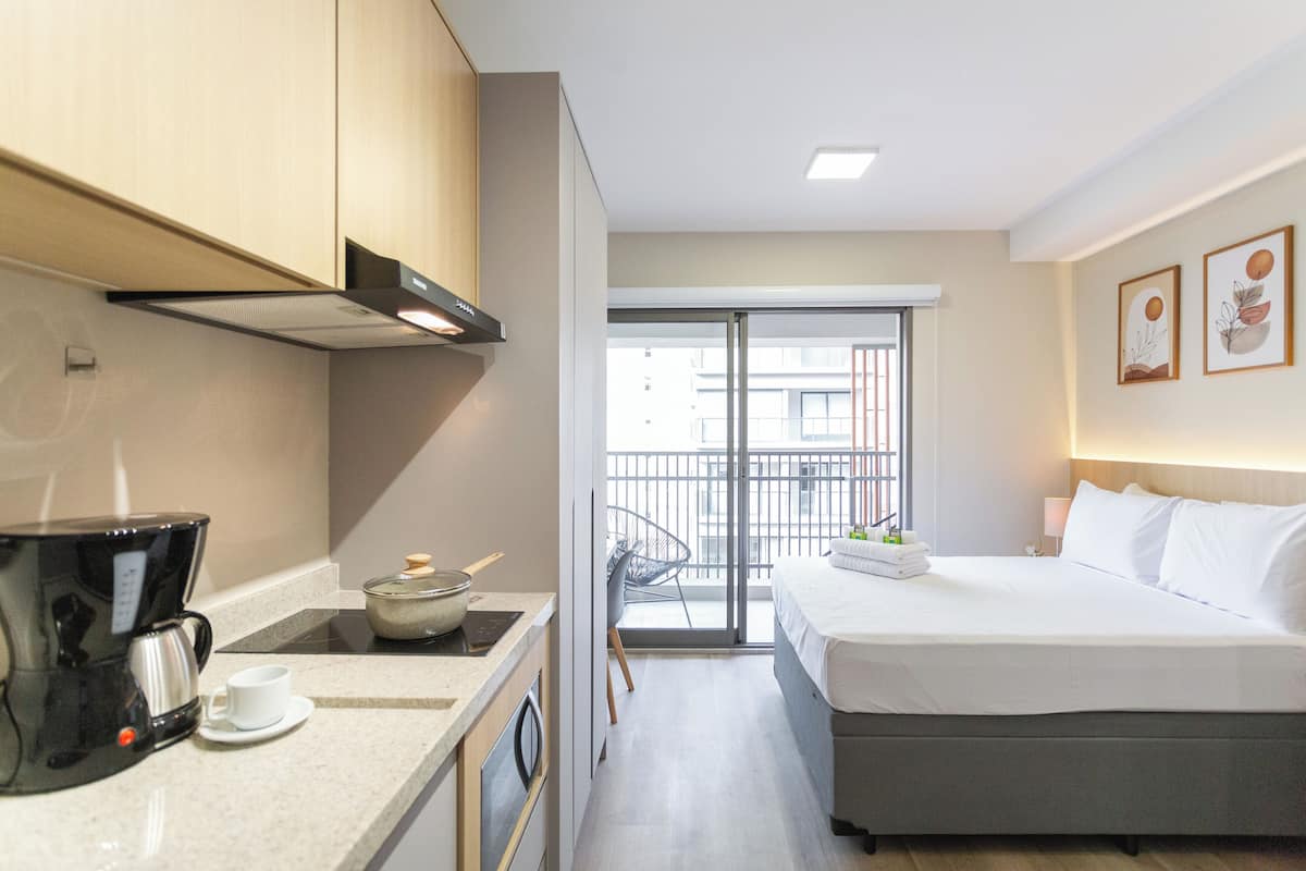 A hotel room with a bed, a coffee maker, a small table, and a view of the outside balcony.