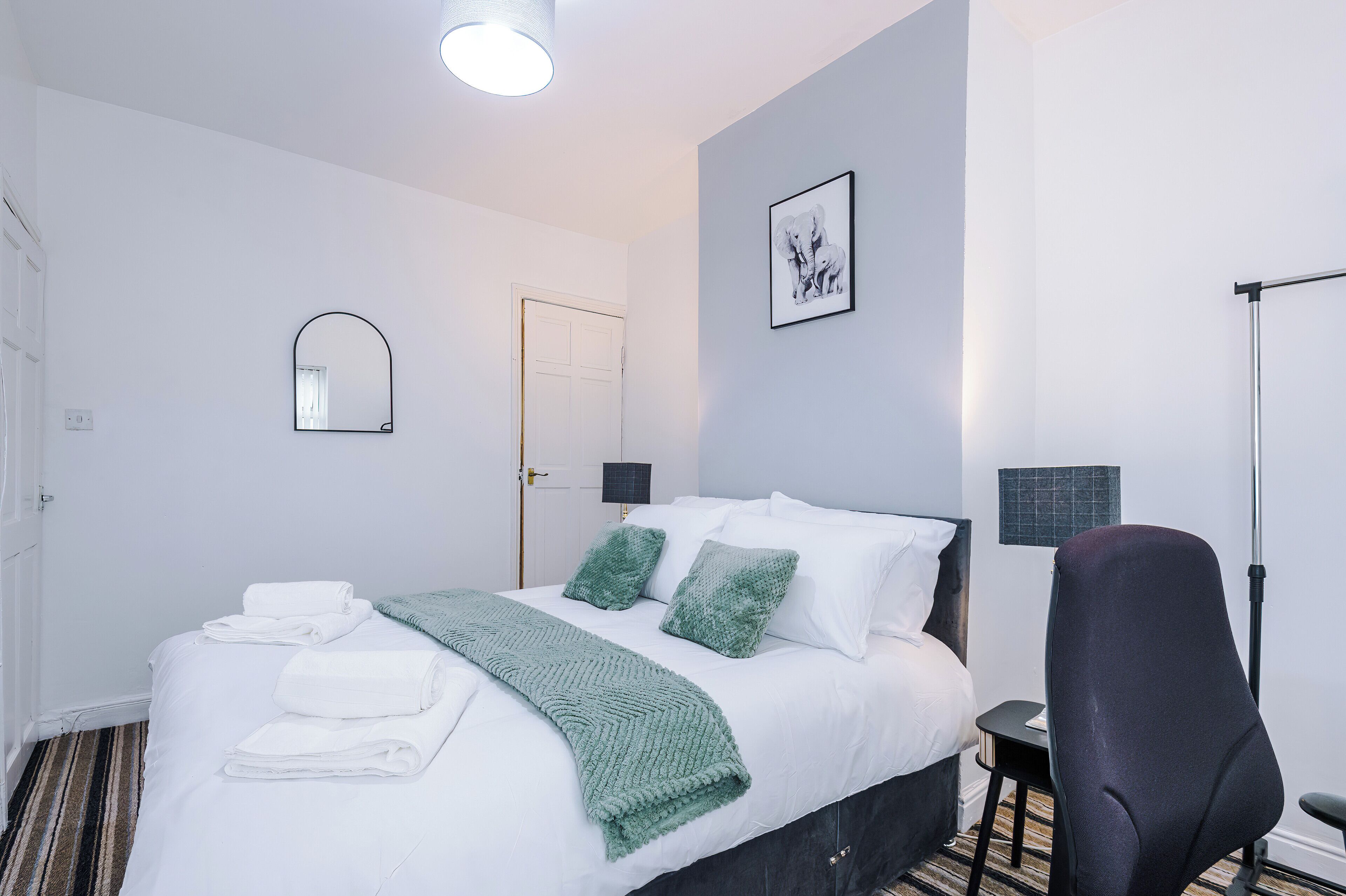 Een hotelkamer met een bed, een stoel, een bureau, een lamp, een spiegel en een ingelijst schilderij aan de muur.