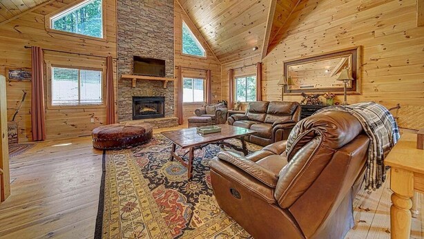 A log cabin interior with a fireplace, leather sofa, and a large mirror.