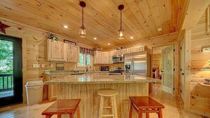 A wooden cabin interior with a kitchen, bar stools, and a large island.