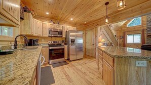 A spacious kitchen with wooden cabinets, stainless steel appliances, granite countertops, and a wooden ceiling.