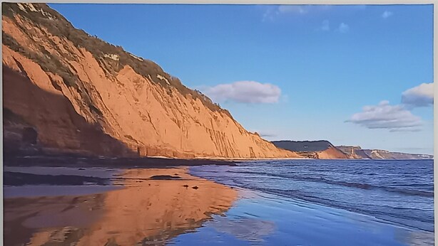 Un paysage côtier avec des falaises et des eaux calmes qui reflètent le ciel.