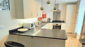 Une cuisine moderne dotée d’un îlot central, de meubles blancs, d’appareils électroménagers en acier inoxydable et de luminaires suspendus.