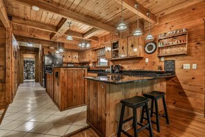 Una cucina rustica con pareti in legno e un'isola centrale, con illuminazione a sospensione e un orologio appeso al muro.